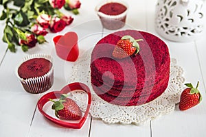 Red cake without cream `red velvet` on a white wooden table, decorated with strawberries, roses and white openwork vase with a hea