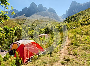 Red camping tent next to trail in mountains