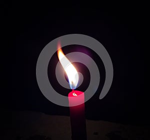 Red candle with beautiful flame and black background selective focus