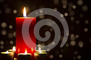 Red Candle with fire against defocused lights in darkness with golden bokeh in the dark Background