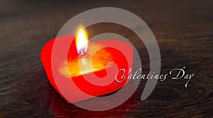 Red candle in the form of a heart on a dark background with the inscription of valentines day. Congratulations on Valentine`s Day