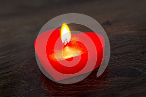 Red candle in the form of a heart on a dark wooden background_