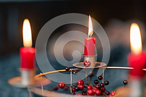 Red candles burning on selfmade Advent wreath made of wire grid decorated with red dried berries with blurred couch living room in