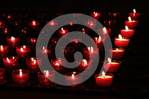 Red candles with glowing lights in darkness in church. Peace and hope background. Religion concept.