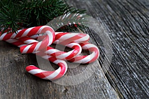 Red candy canes on old wooden table with fir branch.