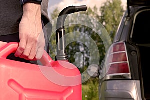 A red canister on the asphalt near the car. The car ran out of gas and stalled. A young man hoping for help on the road