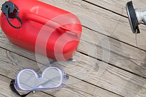 Red canisters with fuel for filling chainsaws, on a wooden background, with eye protection items