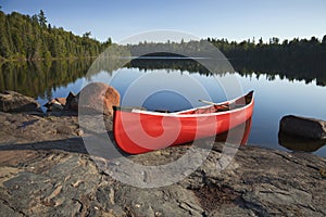 Red Canoe on Rocky Shore of Calm Lake with Pine Trees