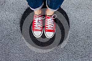 Red canvas sneakers shoes on woman`s feet on the asphalt with black circle