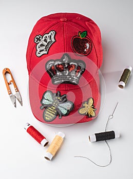 Red cap with various patches, threads, scissors and a neele on white background photo