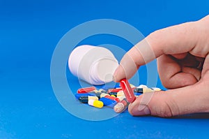 Red capsule in a man`s hand against a background of multi-colored tablets