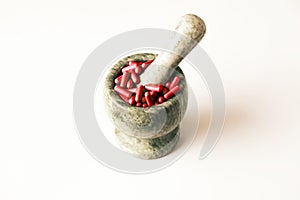Red capsules and orange pills with mortar pestles on white background.
