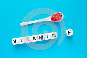 Red capsules in the white spoon and the word vitamin E from whit