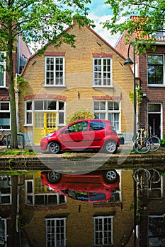 Red car on canal embankment in street of Delft. Delft, Netherlands