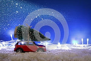 Red car carrying a christmas tree over the snow.