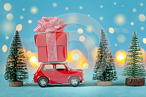 Red car carrying on roof a gift box and Christmas tree on a blue background. Christmas holiday concept