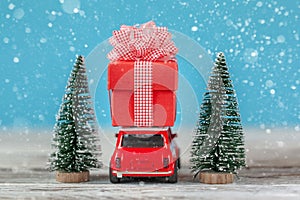 Red car carrying on roof a gift box  and Christmas tree on a blue background. Christmas holiday concept