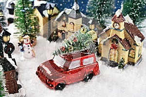 A red car with Christmas tree on the roof in the middle of the street in the small town on snowy night