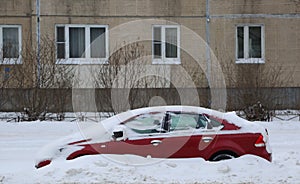 Red car covered with white snow is parked at a residential building