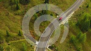 Red car drives on curvy road winding on slopes with forests