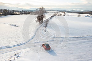 Red Car Driving Down Snow Covered Road, Winter Journey Through Scenic Landscape