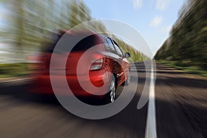 Red car driving at high speed on asphalt road outdoors, motion blur effect