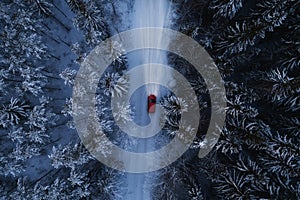 Red car driving on winter mountain road at night time. Beautiful aerial view with the trees covered in snow.
