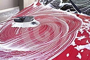 Red car front hood washed in self serve carwash, detail on brush leaving strokes in white soap foam