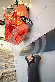 Red car hags on wall and man looks up in photo