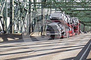 Red car hauler big rig semi truck transporting cars on the two hydraulic semi trailers driving on the arch sectional bridge