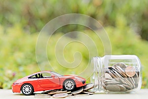 Red car on jar of coin on blurred green natural background. Saving money and investment concept
