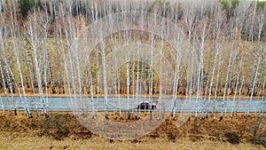 Red car moving through autumn forest along trees. Aerial view of driving