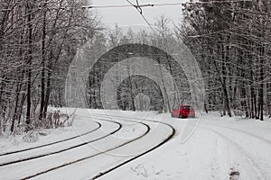 Red car near the tram line rails in the snow-covered forest in Kiev. Ukraine