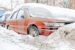 Red car parked in snowdrift. Old rusty auto covered in snow. Wheel stuck in the deep snow