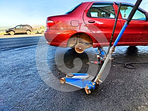 A red car with a punctured wheel and a jack for its repair on the asphalt outdoors on a city street. Car repair service