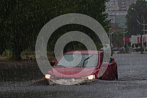 Red car rides in heavy rain on a flooded road