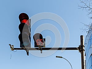 Red car traffic light and countdown timer installed on a pole above a roadway on a city street against a blue sky