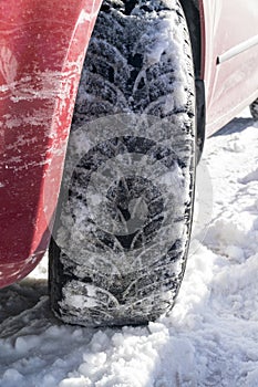 Red car with winter tires on a snowy road, closeup.
