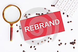 A red card with text REBRAND on a white background next to a magnifying glass and scattered coffee beans