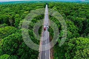 Red cargo truck drives on an asphalt highway through a green forest.