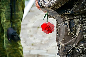 Red carnation flowers in the hand of men in camouflage uniform