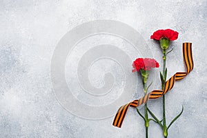 Red carnations and St. George ribbon on a concrete background. Symbol may 9, victory day Copy space