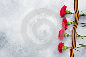 Red carnations and St. George ribbon on a concrete background. Symbol may 9, victory day Copy space