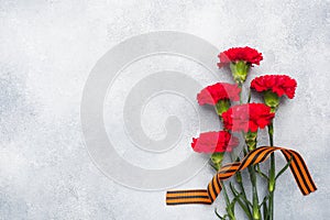Red carnations and St. George ribbon on a concrete background. Symbol may 9, victory day Copy space