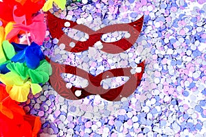 Red carnival costume mask in colorful confetti and streamers on pink background with space for text photo