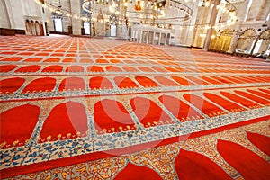 Red carpets with traditional patterns on floor of 16th century Suleymaniye Mosque with bright lights