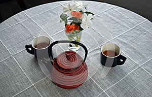 Red Cast Iron Teapot with Black Cups and Orange and White flowers on a gray background