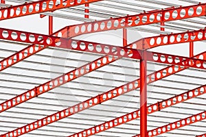 Red castellated beam metal roof structure of large industrial building in construction site against white cloudy sky background