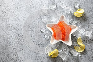 Red caviar in bowl in shape of star served with lemon and ice cubes for party