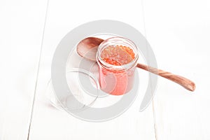 Red caviar in glass bowl and spoon on white wooden background
